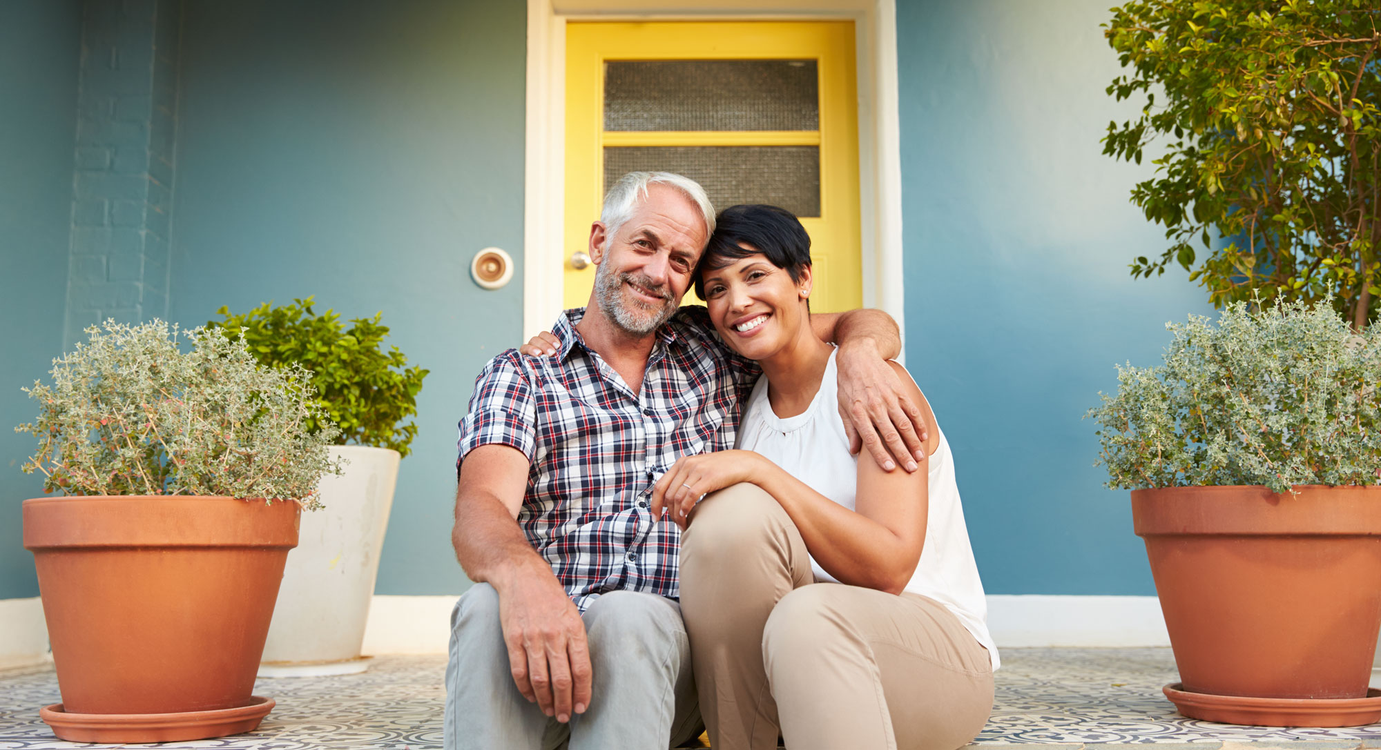 Retired couple seated on their porch smile at camera