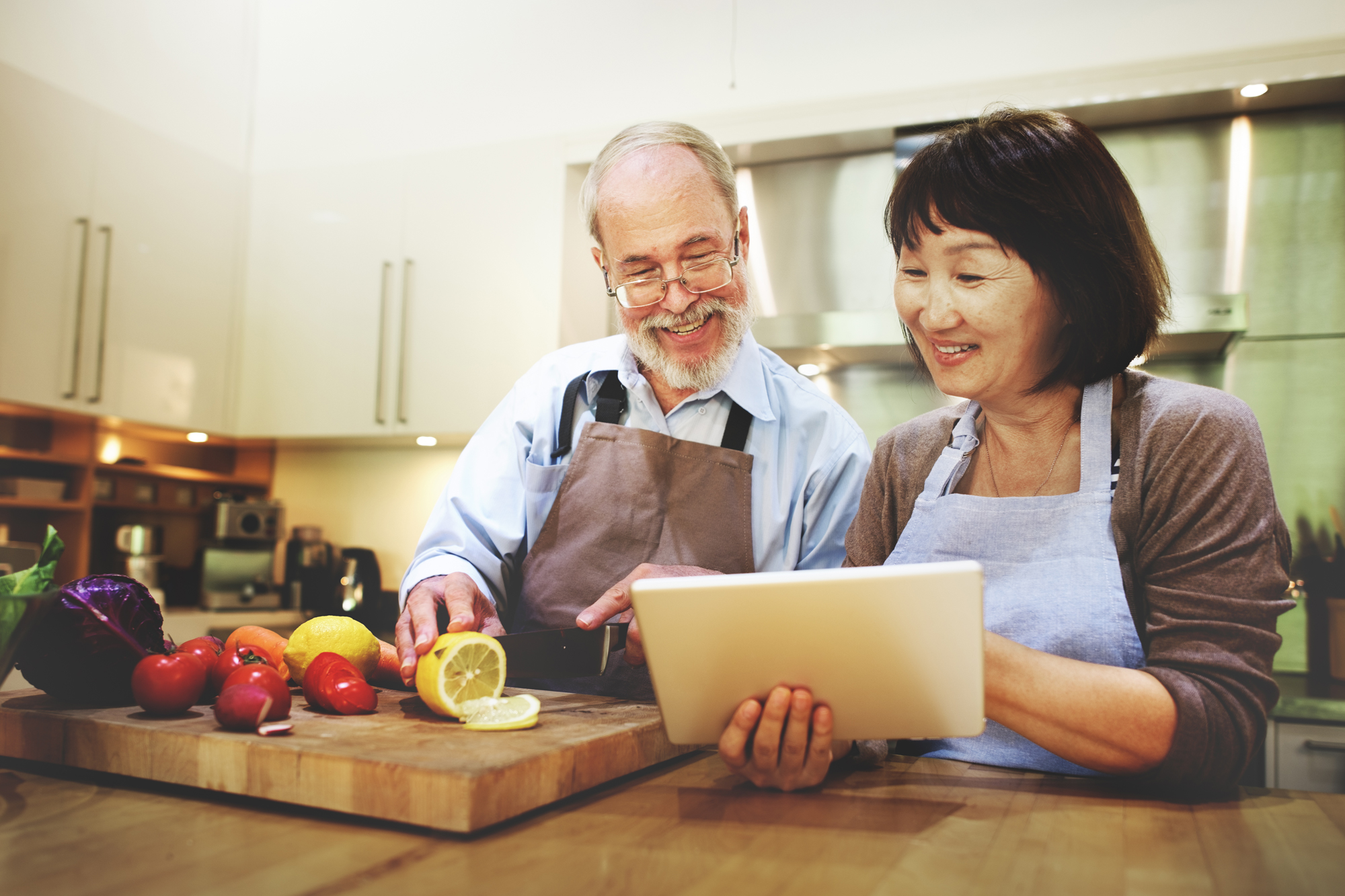 Retired couple slicing fruit and looking at tablet