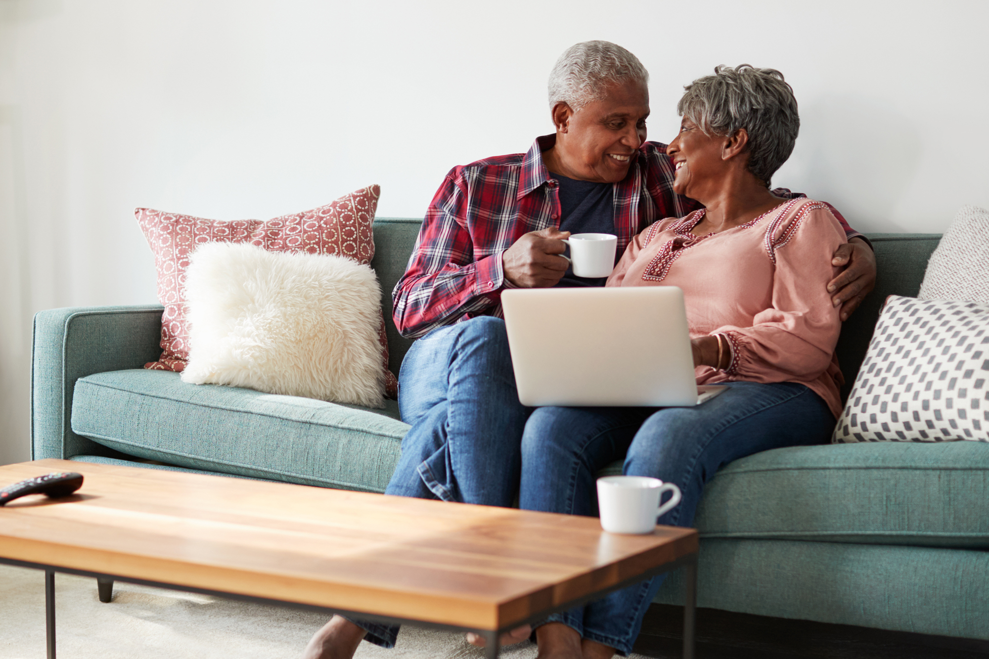 Retired couple seated on couch with laptop and coffee smiling at each other