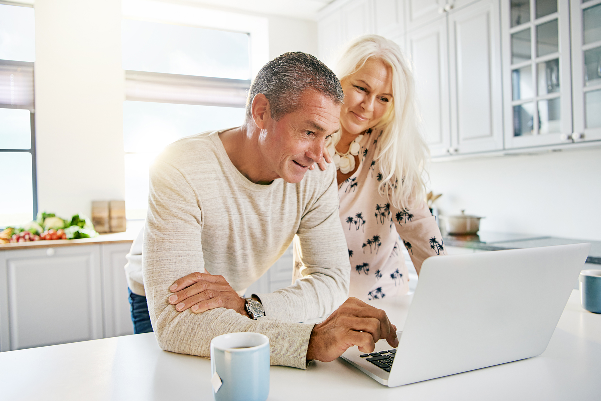 Retired couple standing in kitchen looking at laptop